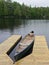 Canoes tied to a wooden dock on a lake surrounded by evergreen trees