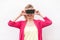 Cant see you! Portrait of happy modern young woman in pink blouse standing, holding and covering eyes with smartphone, like