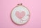 Canvas with embroidered heart and needle in hoop on pink background, top view