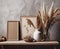 Canvas frames and vases with pampas grass on wooden table near grunge stucco wall. Boho interior design with home decor. Created
