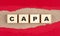 CAPA word on wooden cubes on red torn paper , financial concept background