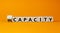 Capacity or incapacity symbol. Turned a wooden cube and changed the word `incapacity` to `capacity`. Beautiful orange backgrou