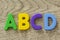 Capital letters A B C D in flat colorful plastic letter toys on gray wooden background