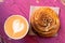 Cappuccino and cinnamon pastry roll isolated on peeling and cracked pink painted wood from above