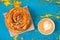 Cappuccino and cinnamon pastry roll  on peeling and cracked blue and yellow painted wood from above. Space for text
