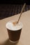Cappuccino coffee with vanilla crumbs in a brown disposable paper cup with a straw. vertical view
