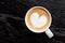 Cappuccino with heart shape foam in a white ceraamic mug isolated on dark brown wood table with grain from above. Space for text