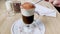 Cappuccino, latte with froth milk in cup. Spoon scoops whipped cream, sprinkled with ground cinnamon and cocoa powder, from tall