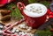 Cappuccino with marshmallow in red mugs and fir-tree branches, striped stick candys, fir cones on wooden table.