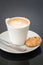 Cappuchino or latte coffe in a white cup and a biscuit on a dark background