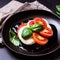 Caprese salad on a black plate. Tomatoes, mozzarella cheese and basil