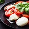 Caprese salad on a black plate. Tomatoes, mozzarella cheese and basil