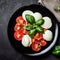 Caprese salad on a black plate. Tomatoes, mozzarella cheese and basil. Top view