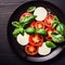 Caprese salad on a black plate. Tomatoes, mozzarella cheese and basil. Top view