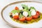 Caprese salad with fresh cherry tomatoes mini mozzarella pesto basil olive oil and balsamic sauce on a white plate and on a