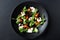 Caprese salad with mozzarella, tomato, basil and balsamic vinegar arranged on black plate and dark background. Top view