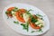 Caprese salad on a white plate. Large slices of tomatoes, mozzarella cheese and basil greens