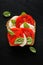 Caprese sandwich, slice of bread with fresh tomatoes, mozzarella cheese, basil leaves and olive oil on a black background