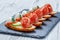 Caprese sandwiches with tomato, mozzarella cheese, basil, salami on ciabatta bread on stone slate background close up.