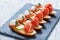 Caprese sandwiches with tomato, mozzarella cheese, basil, salami on ciabatta bread on stone slate background close up.