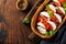 Caprese traditional italian salad in olive wooden bowl on old rustic background.