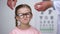 Capricious little girl rejecting eyeglasses from optician, feels insecure, shy