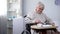 Capricious senior lady in wheelchair eating with disgust unappetizing dinner