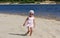 Capricious and unhappy caucasian child of three years in sunglasses walking on the sand river beach