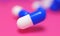 Capsule medicine pills, health pharmacy concept. Drugs for treatment medication. Heap of blue white color capsules on pink backgro