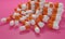 Capsule medicine pills, health pharmacy concept. Drugs for treatment medication. Heap of orange white color capsules on pink backg