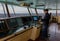 The captain with a blue cap on the bridge of his cargo ship at sea.