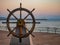 Captains steering wheel or rudder of an old wooden sailing ship in a port at sunset