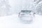 Car covered in snow driving in snowstorm on a cold winter day in the forest