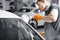 Car detailing - male worker holds a polisher in the hand and polishes white car in auto repair shop.