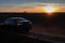 car drives along a country road in the evening against the backdrop of a beautiful orange sunset