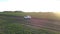 Car drives along ground road past fields at bright sunset