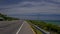 Car Drives along Highway Past Ocean Beach and Hilly Landscape