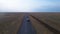 Car drives on deserted road in the middle of harvested agricultural fields in countryside, drone shooting from height