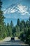 A car drives down the tree lined road with Mt. Shasta, a volcanic formation in Northern