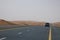 A car drives on an empty road in the deserts of Dubai, UAE