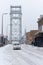 Car drives on snowy road near Boskoop lift bridge. Pedestrians on the side of the road