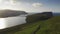 Car driving along coastal road view on wild green island at sunset.Cinematic rear view approaching.Faroe Island road