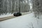 Car driving on asphalt road through the forest covered in snow