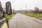 The car is driving on a muddy, rain-washed road. You can see the car mirror.