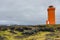 The car in front of orange lighthouse on the rocks in Iceland,