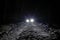 The car goes on a snowy road on a dark black night in winter. Headlights brightly illuminate the path and the forest after a