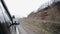 A car going on a curvy road near the hills. Reflection of young female passenger in wing mirror.