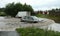 A car going through the flooded road beside a cargo truck with stalled engine in water