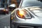 car headlight on the background of the city and the road, Modern silver car parking on the road. Close up. Headlights detail, AI