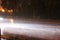 Car headlight illuminates rain in the dark on the track